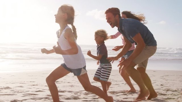 Parents Chasing Children Along Beach On Summer Vacation