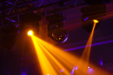 Disco ball and light projectors at night party, warm yellow light stream