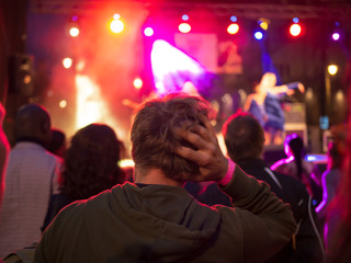 Lonely sad young man in the crowd watching a concert, hand on head.