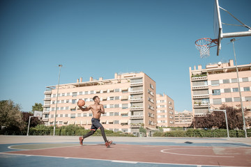 Afroamerican young man playing street basketball in the park