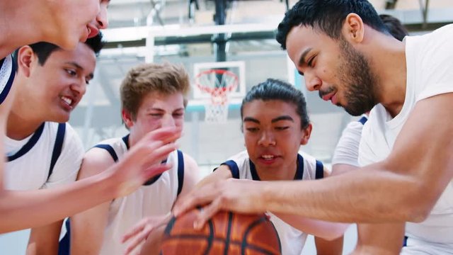 Male High School Basketball Players Joining Hands On Ball During Team Talk With Coach