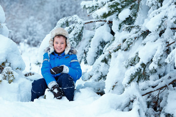 Cute little boy wearing warm clothes playing on winter forest