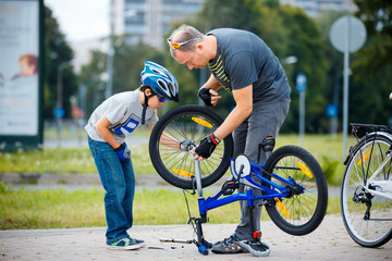 Cute little boy with his father repairing bicycle outdoors