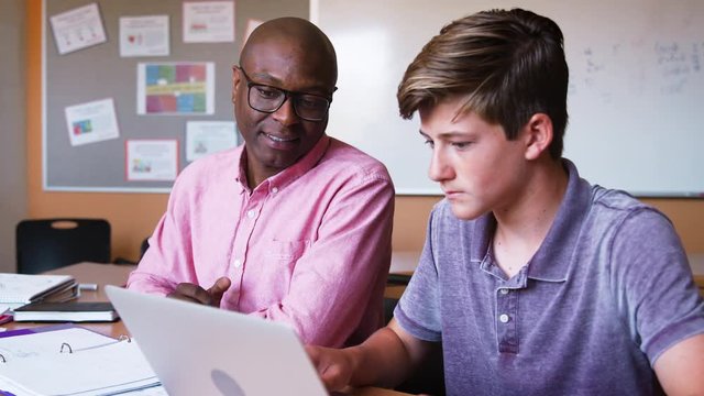 High School Tutor Giving Male Student Using Laptop One To One Tuition At Desk