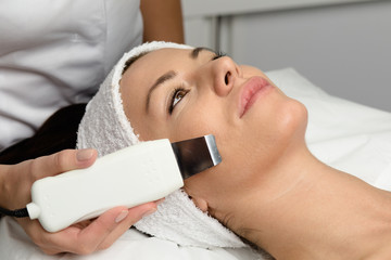 Beautiful woman receiving ultrasound cavitation facial peeling. Skin cleansing procedure at beauty spa salon.
