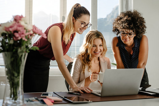 Three businesswomen looking at laptop and smiling