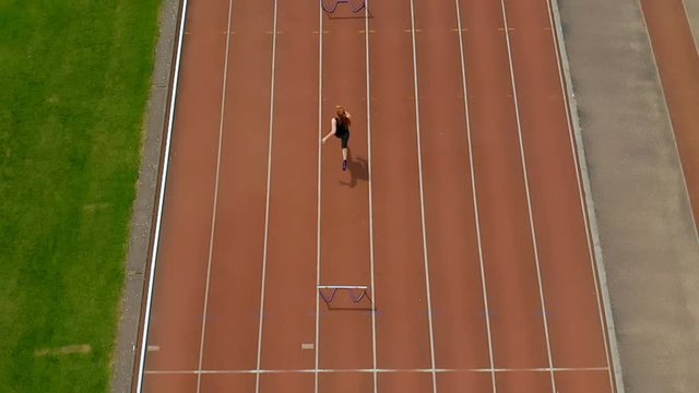 Female athletic jumping over hurdle on sports track 4k