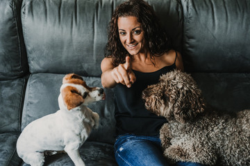 Young beautiful woman playing with her dogs in her sofa at home. Having fun together. Pet friendly. Lifestyle.