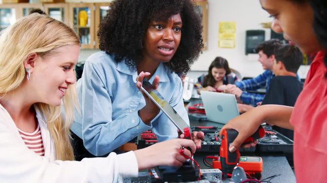 High School Teacher With Female Pupils Building Robotic Vehicle In Science Lesson
