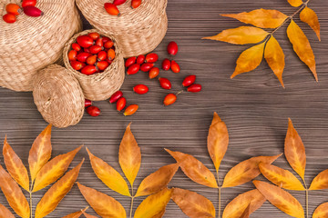Rose hips in a basket and yellow leaves on a wooden surface. Concept of autumn background