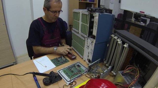 Engineer at Work in the Office / Engineer with digital multimeter solves problem on the electronic printed circuit board