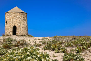 Fototapeta na wymiar Old windmill in blue sky. The old windmill is located on Gira beach, Lefkada Island, Greece