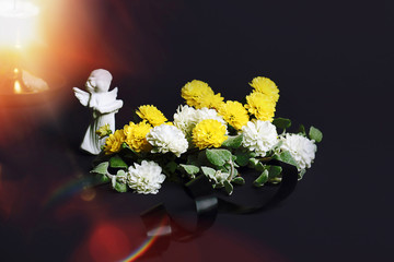The concept of mourning. White and yellow flowers on a dark background, an angel and a candle. We remember, we grieve. Selective focus, place for text.
