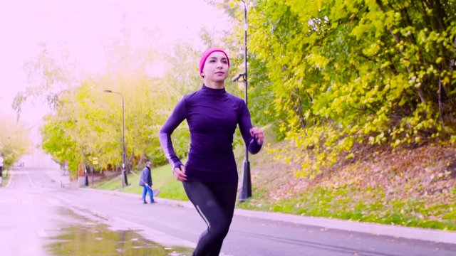 Dolly shot, slow motion. Young woman running in the park at autumn day