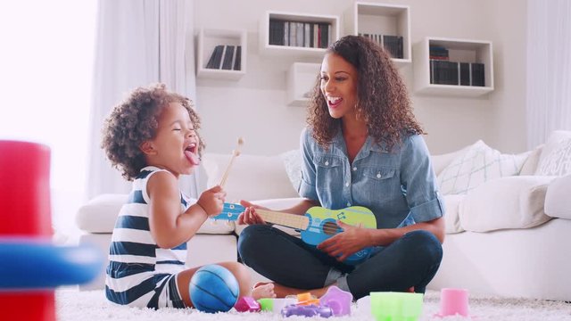 Young black girl playing xylophone with mum in sitting room