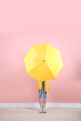 Woman hiding behind yellow umbrella near color wall © New Africa