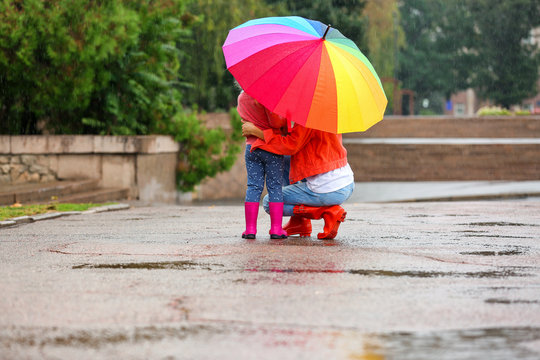 Mother and daughter with bright umbrella under rain outdoors