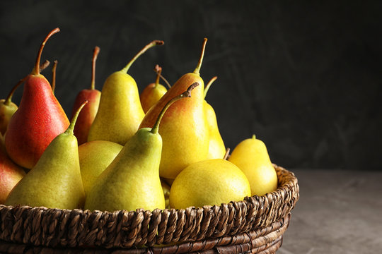 Wicker bowl with ripe pears on table against dark background, closeup