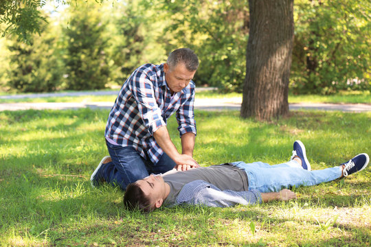 Passerby performing CPR on unconscious man outdoors. First aid