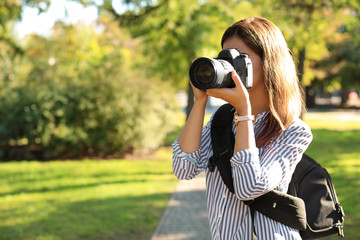 Young female photographer taking photo with professional camera in park. Space for text