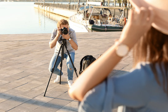 Male photographer taking photo of young woman with professional camera at pier