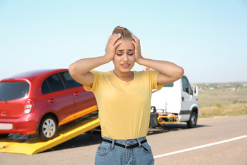 Woman near broken car and tow truck on country road