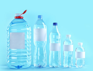 Different bottles of pure water with blank tags on color background