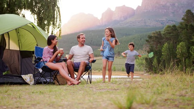 Kids run to join parents sitting by tent in rural setting
