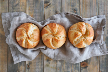Three crusty round bread rolls in a row on linen towel on rustic wooden background