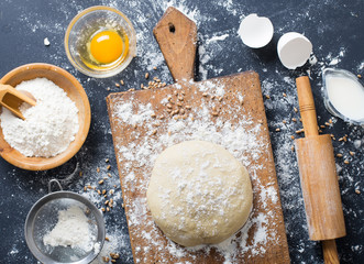 Baking ingredients. Bowl, eggs, flour, eggbeater, rolling pin and eggshells on black chalkboard from above.