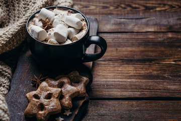 Winter holidays greeting card or poster template. Hot chocolate with marshmallows, traditional gingerbread cookies and knitted blanket. Copy space. Cozy Christmas atmosphere, home weekend concept