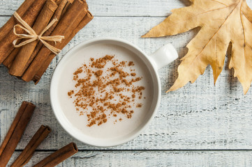 white cup of salep milky hot drink of Turkey with cinnamon powder and sticks healthy spice and autumn winter leaf on white rustic vintage wooden table. Sahlep background
