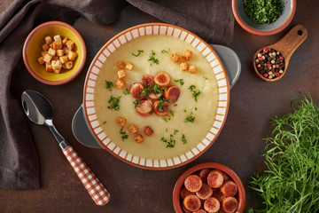 Flat lay of potato cream soup with croutons, fried vienna sausages and green coriander on dark