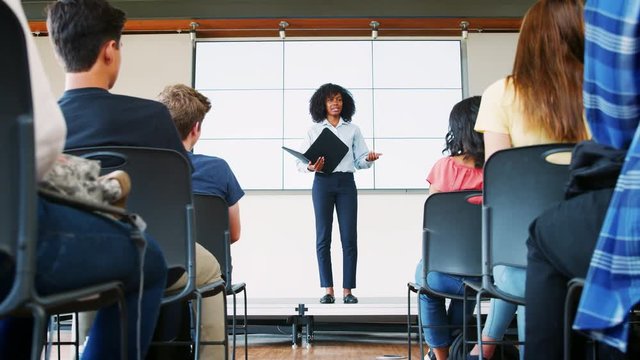 Teacher Giving Presentation To High School Class In Front Of Screen
