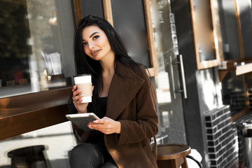 Beautiful girl uses a tablet and drinks coffee, sitting in a cozy cafe.