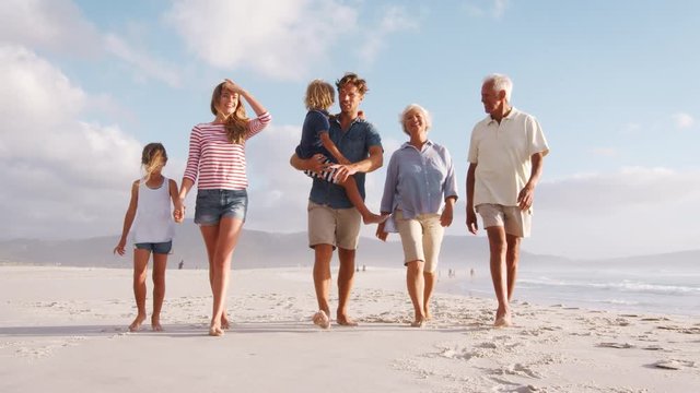 Multi Generation Family On Summer Vacation Walking Along Beach