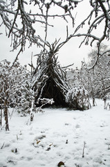 hut of old branches in the snow-covered winter garden