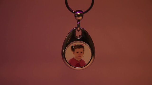 Close Up of the Hanging Child's Photo in Metal Souvenir Keychain. The Light Moves From Left to Right.