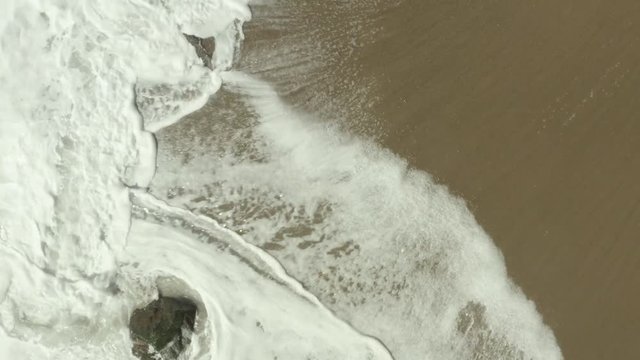 Birdseye view of waves crashing against rocks on the beach.