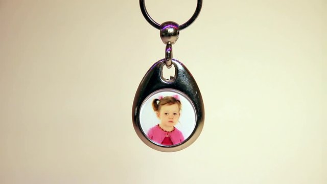 Close Up of the Hanging Child's Photo in Metal Souvenir Keychain. The Light Moves From Right to Left.