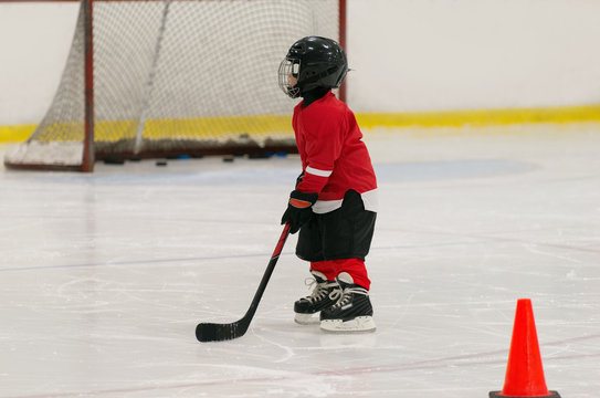 The little hockey child is training on ice wearing in full hockey equipment: helmet, gloves, skates,   stick. 