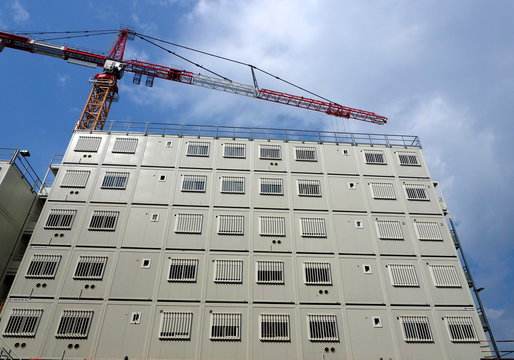Modern modular container building at a construction site with a large tower crane under a blue sky