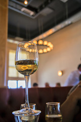 Бокал белого вина стоит на столе на фоне люстры.вертикально.