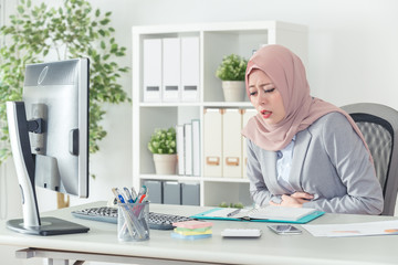 muslim businesswoman having stomachache at work