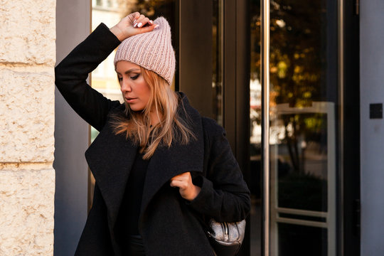 Fototapeta beautiful young model in pink knitted hat standing do to work, on background mirrow wall on  sunny autumn day in  big city. Autumn warm photo.Woman smiling and look away, joyful cheerful mood.