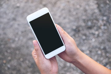Mockup image of hands holding white mobile phone with blank black screen with street background