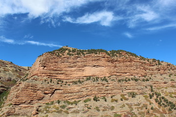 rock cliff face under the blue sky. Utah has some very scenic landscapes and views like this, green shrubs and bushes on top give it a hint of color from the top of the cliff.