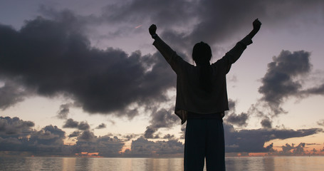Silhouette of woman raising hand at sunrise time