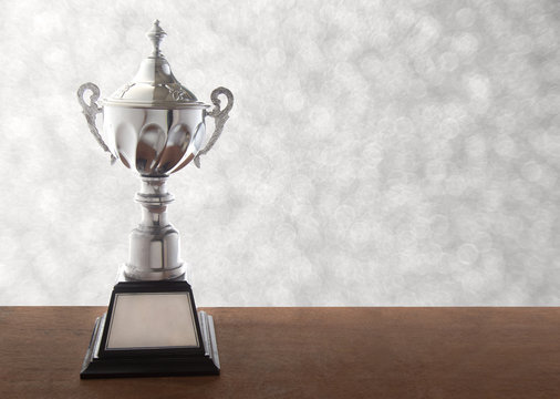 Silver trophy on wooden table over abstact white bokeh background. Winning awards with copy space.