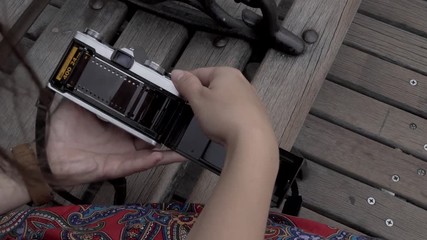 Female hands loading a film into an old analog camera on a street bench - Powered by Adobe